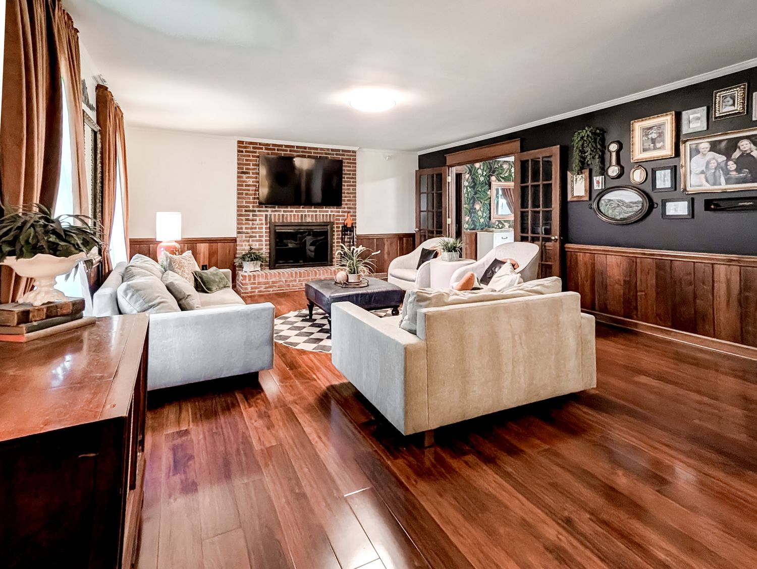 Family room with a floor-to-ceiling brick fireplace, mounted TV, walnut wainscoting, grey sofas and rich hardwood floors
