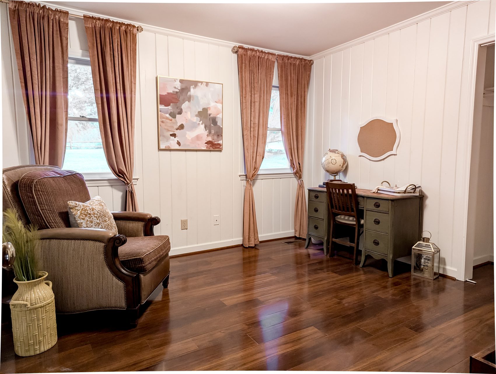 Bright bedroom with white vertical board-and-batten paneling, dusty-rose curtains, hardwood floors and a writing desk